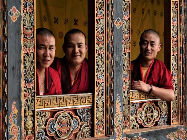 Three Buddhist monks from Bhutan wearing maroon robes smiling